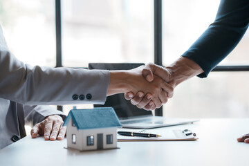 Real estate agent shakes hands with a client to sign a home purchase contract congratulating the client on the purchase.
