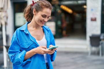 Young woman smiling confident using smartphone at street