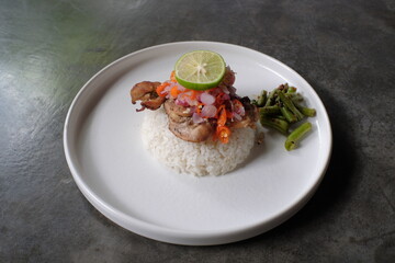 Delicious lunch menu, white rice, chicken meat with chili sauce topping, sliced chili, onion, lemongrass leaves, orange leaves, and others.