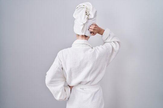 Blonde caucasian woman wearing bathrobe backwards thinking about doubt with hand on head