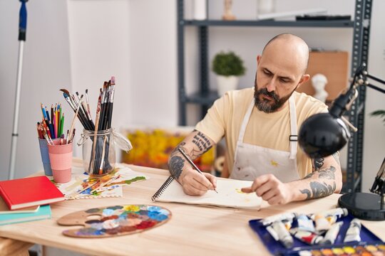 Young bald man artist drawing on notebook at art studio