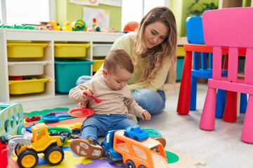 Teacher and toddler playing with cars toy sitting on floor at kindergarten