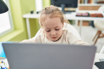Adorable blonde girl student using laptop sitting on table at classroom