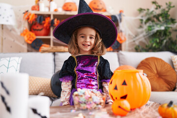 Fototapeta premium Adorable hispanic girl having halloween party putting sweets on pumpkin basket at kindergarten