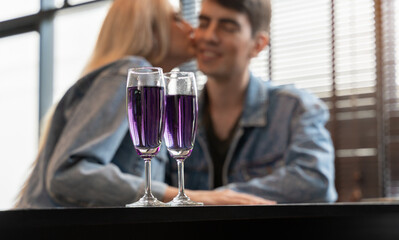 Glasses of purple cocktail with blurry happy loving couple at bar