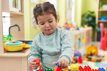 Adorable hispanic toddler playing with construction blocks standing at kindergarten