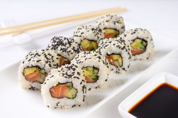 Sushi roll California with salmon, sesame seeds, avocado, cream cheese on white background. Sushi menu, rolls served on white dish and soy sauce. Traditional Japanese cuisine food.