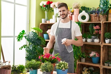 Young caucasian man florist using diffuser watering plant at flower shop