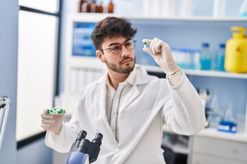 Young hispanic man scientist holding pills at laboratory
