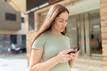 Young beautiful woman using smartphone with serious expression at street