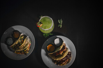 Platos con deliciosas tortillas vegetarianas y un cocktail de autor sabor limón, menta, jengibre. Ángulo cenital, fondo negro