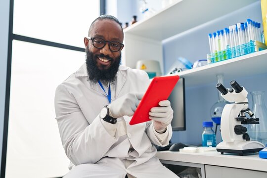 Young african american man wearing scientist uniform using touchpad at laboratory