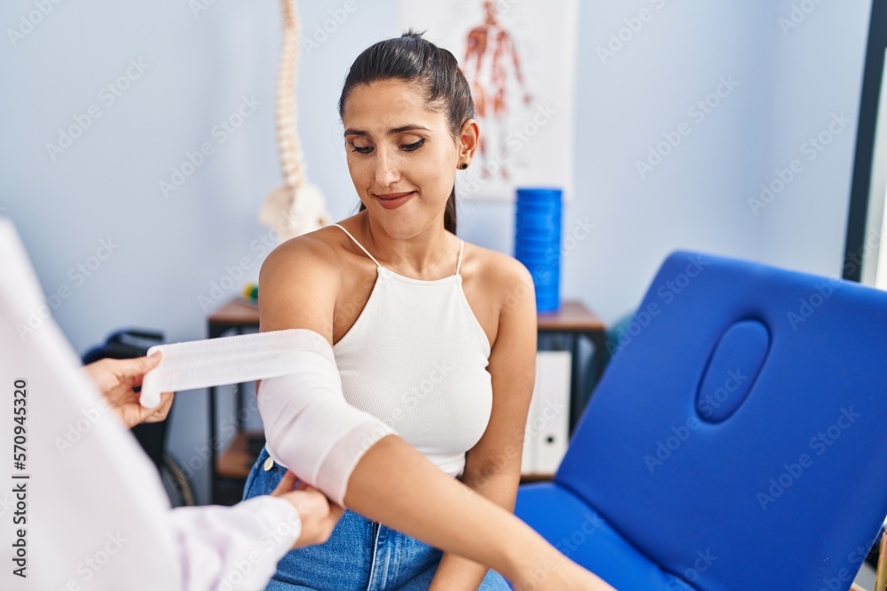 Canvas Prints Young hispanic woman smiling confident bandaging arm at physiotherapy clinic