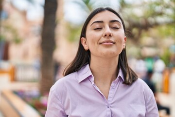 Young hispanic woman smiling confident breathing at park