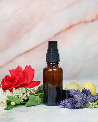 Fototapeta na wymiar Floral face and body mist in amber spray bottle with lavender, rose, lemon, jasmine and elderflowers on marble background. 