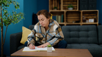 Fototapeta na wymiar Middle age hispanic woman writing on notebook sitting on sofa at home