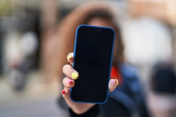 Young beautiful hispanic woman showing screen app at street