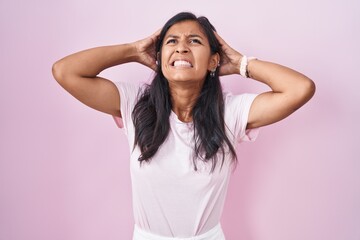 Young hispanic woman standing over pink background crazy and scared with hands on head, afraid and surprised of shock with open mouth