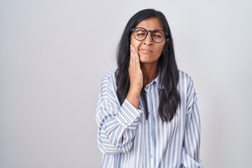 Young hispanic woman wearing glasses touching mouth with hand with painful expression because of toothache or dental illness on teeth. dentist