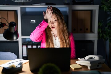 Young caucasian woman working at the office at night surprised with hand on head for mistake, remember error. forgot, bad memory concept.