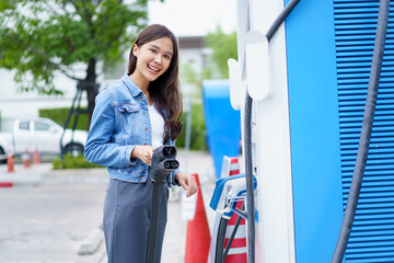 Unrecognizable Asian woman holding the CCS 2 EV charging connector at EV charging station.