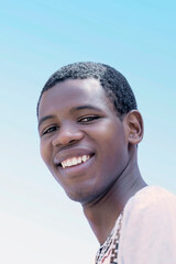 Portrait of a laughing young man wearing a traditionnal white shirt, 19 years old, outdoors, sunny day, blue sky, photo