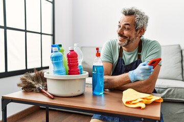 Middle age grey-haired man using smartphone cleaning table at home