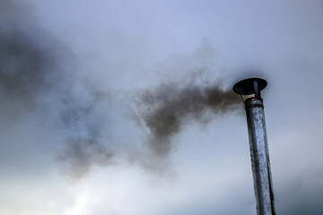 Iron pipe blows black smoke against the sky	
