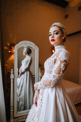 A beautiful bride model in a white lace dress is standing in a hotel room, reflected in the mirror....