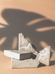 Product showcase. Stone podium. Nature stage. Cracked concrete rock pieces pile scene palm leaf shadow on beige copy space advertising background.