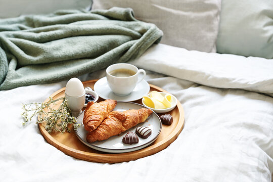 Mothers day breakfast served with love on bed. Coffee, croissant, egg and chocolate hearts on a wooden tray. Natural bed cloth. Also for birthday, valentines or fathers day, copy space