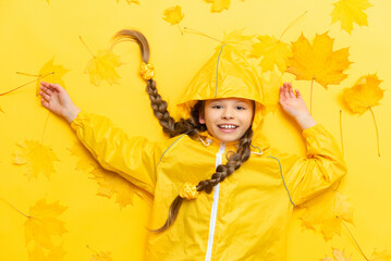 A child in a waterproof raincoat against the background of maple leaves in the autumn season.