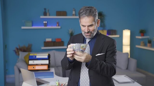 Funny and entertaining businessman counts the money he earns, the businessman who earns a lot rejoices.
Fun and likeable mature business man counting dollars earned at home, happy and winning man.
