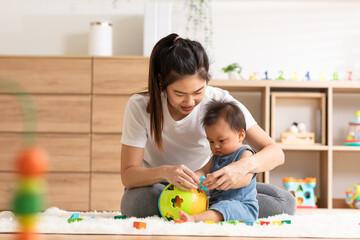 Obraz na płótnie Canvas Asian mom teaching baby boy learning and playing toys for development skill at home or nursery room. Happiness mother and baby spending time together at warmth place. Good moment with mom and baby