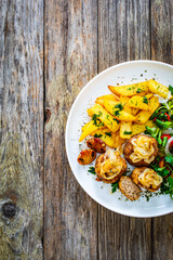 Fried pork meatballs with fried onion, french fries and fresh vegetables on wooden table
