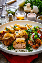 Fried pork meatballs with fried onion, french fries and fresh vegetables on wooden table
