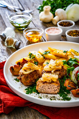 Fried pork meatballs with fried onion, french fries and fresh vegetables on wooden table

