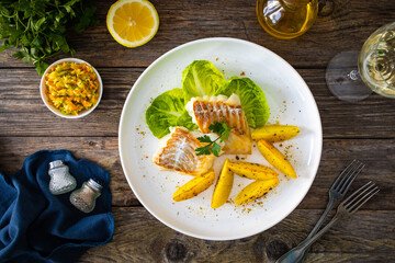 Fish dish - fried cod with baked potatoes and fresh vegetables on wooden table
