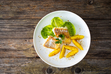 Fish dish - fried cod with baked potatoes and fresh vegetables on wooden table
