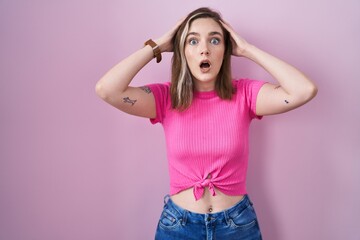 Blonde caucasian woman standing over pink background crazy and scared with hands on head, afraid...