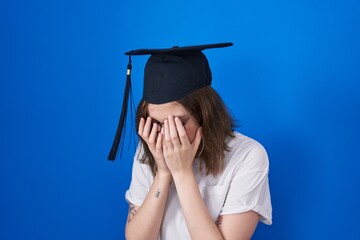 Blonde caucasian woman wearing graduation cap with sad expression covering face with hands while crying. depression concept.