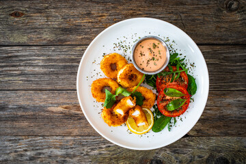 Fried breaded calamari rings with lemon and fresh vegetables on wooden table
