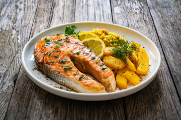 Fried salmon steak with French fries and fresh vegetable salad served on wooden table
