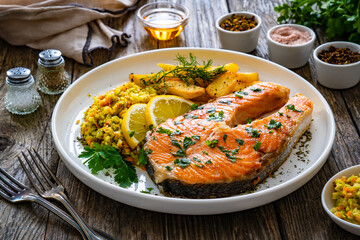 Fried salmon steak with French fries and fresh vegetable salad served on wooden table
