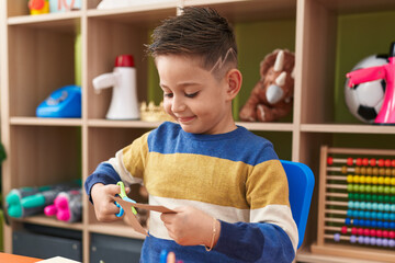 Adorable hispanic boy student smiling confident cutting paper at kindergarten