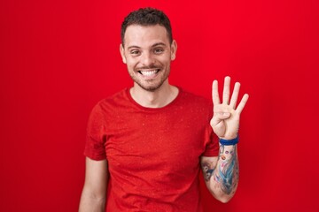 Young hispanic man standing over red background showing and pointing up with fingers number four while smiling confident and happy.