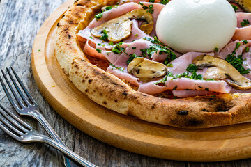Circle prosciutto burrata pizza with mushrooms on wooden table
