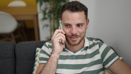 Young caucasian man speaking on the phone sitting on the sofa at home