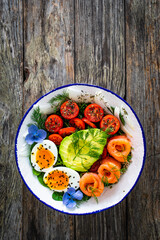 Salmon salad - smoked salmon, hard boiled eggs, avocado and leafy greens on wooden table
