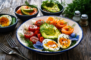Salmon salad - smoked salmon, hard boiled eggs, avocado and leafy greens on wooden table
